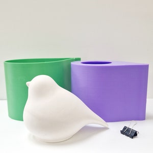 May include: A white ceramic bird figurine with a green and purple silicone mold. The mold is shaped like a bird and a leaf.