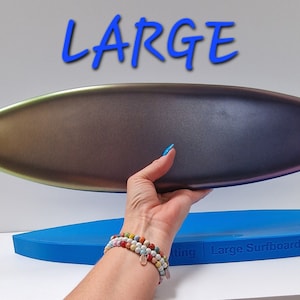 May include: A large, metallic surfboard with a gradient finish, held by a hand. The board transitions from gold to purple. The word "LARGE" is written in blue above the board. A blue surfboard is in the background.
