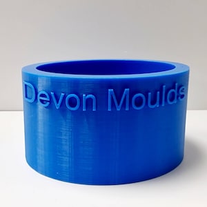 Op de afbeelding: Een helderblauwe cilindrische mal met de tekst "Devon Moulds" in reliëf op de zijkant. De mal heeft een glad, afgerond interieur en een dikke wand. Dit product is ontworpen voor het creëren van diverse vormen.