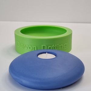 Może przedstawiać: Tealowy niebieski świecznik w kształcie płaskiego kamienia z małym okrągłym wgłębieniem na świeczkę typu tealight. Świecznik stoi na zielonej silikonowej formie z wytłoczonym napisem "Devon Dotting" na boku.