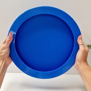 Puede incluir: Una bandeja redonda de color azul brillante con un borde elevado. La bandeja está hecha de plástico y es perfecta para servir aperitivos o bebidas.