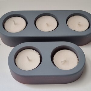 May include: Two gray ceramic candle holders. The larger holder has three candle wells and the smaller holder has two candle wells.