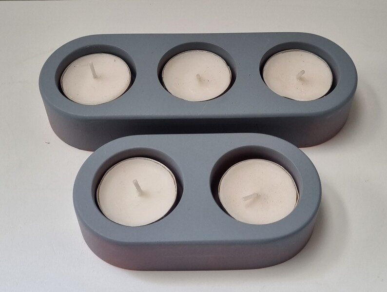 May include: Two gray ceramic candle holders. The larger holder has three candle wells and the smaller holder has two candle wells.
