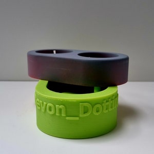 May include: A two-piece candle holder set. The top piece is a dark gray with a slight purple hue. The bottom piece is a bright green and has the text "Devon_Dottie" printed on the side.