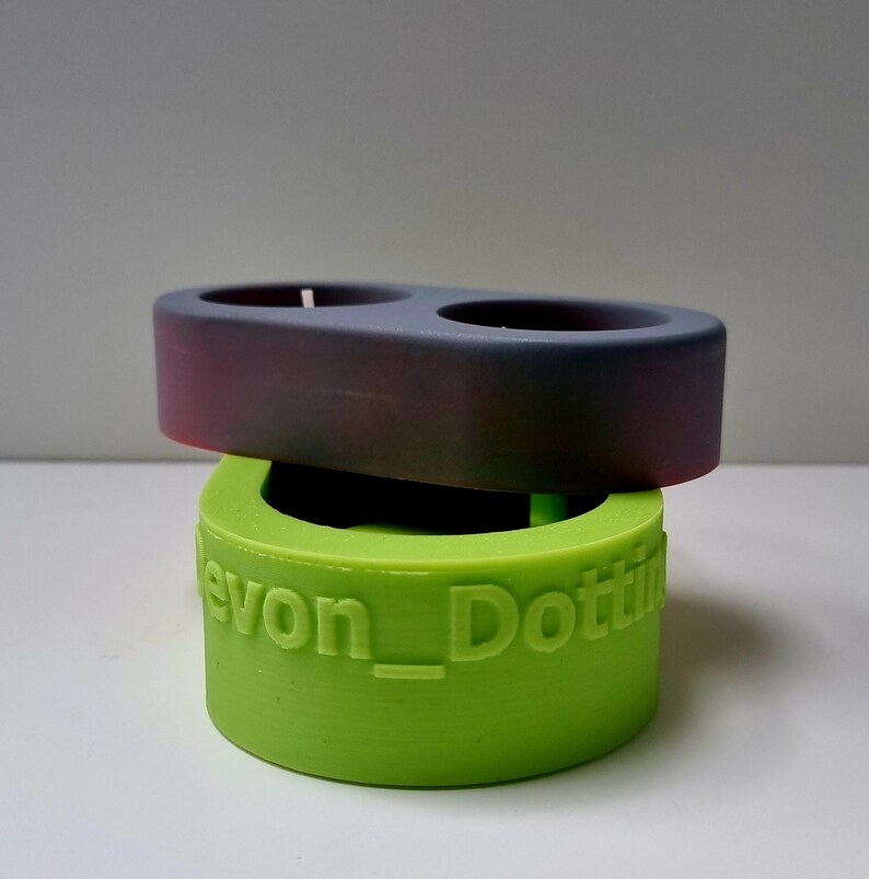 May include: A two-piece candle holder set. The top piece is a dark gray with a slight purple hue. The bottom piece is a bright green and has the text "Devon_Dottie" printed on the side.