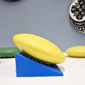 Puede incluir: Un plato de cerámica amarillo se encuentra sobre una cuña de goma azul. El plato está ligeramente inclinado, dando la impresión de movimiento.