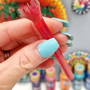 May include: A red plastic paint bottle tip with a clear plastic cap. The tip is split in two, revealing the red paint inside.