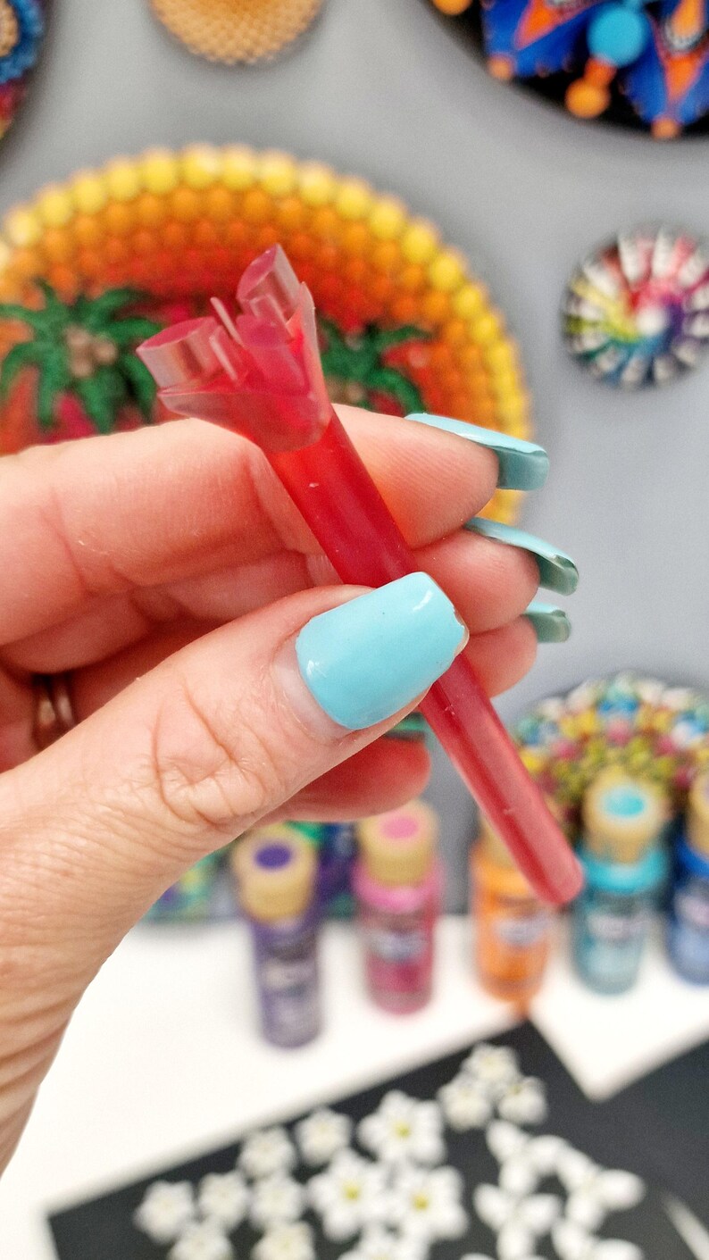 May include: A red plastic paint bottle tip with a clear plastic cap. The tip is split in two, revealing the red paint inside.