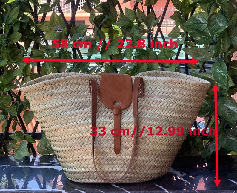 May include: Woven straw tote bag with brown leather accents. The bag measures 22.8 inches wide and 12.99 inches high. Features a leather flap closure and straps. Ideal for carrying items.
