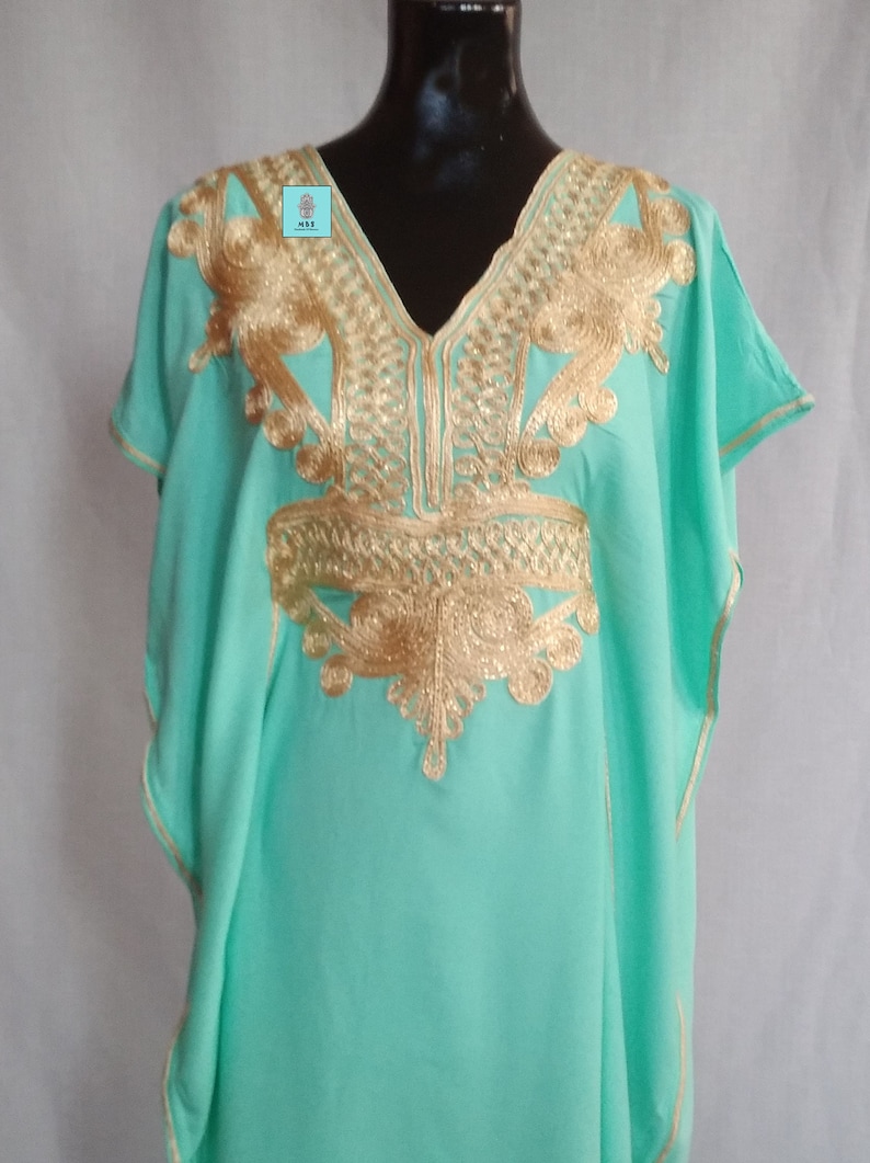 Puede incluir: Una kaftan verde menta con bordados dorados. El bordado presenta un patr&oacute;n geom&eacute;trico y motivos florales.