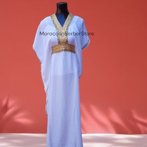 May include: A white maxi dress with gold embroidery around the neckline and waist. The dress has a loose, flowing fit and is perfect for a casual summer look.