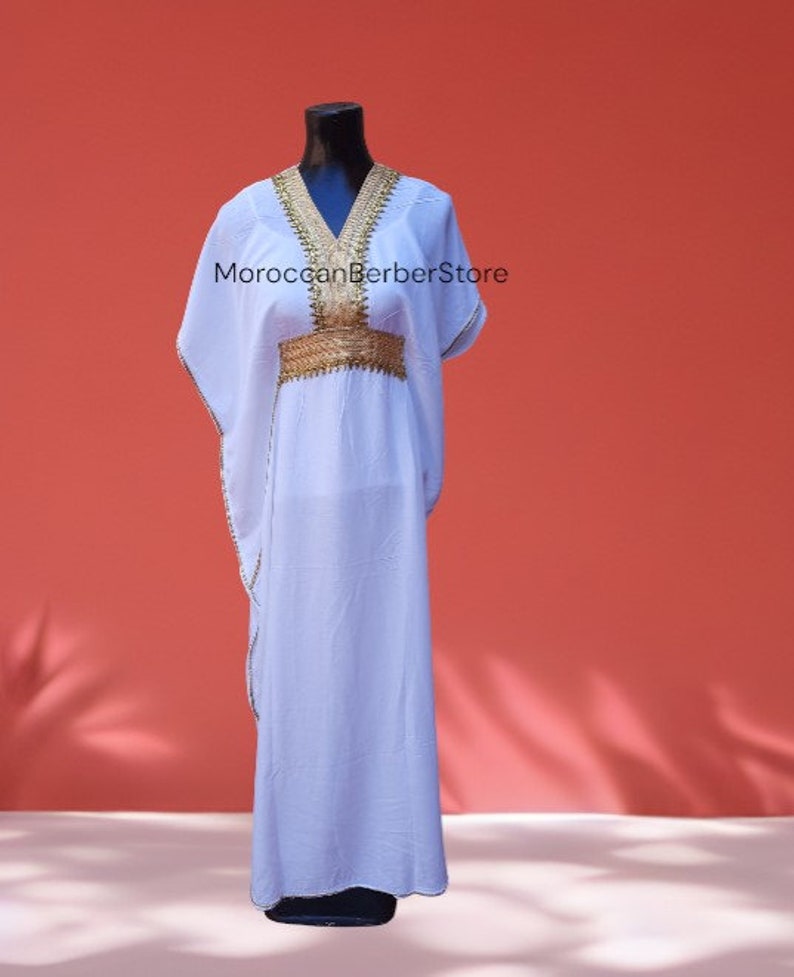 May include: A white maxi dress with gold embroidery around the neckline and waist. The dress has a loose, flowing fit and is perfect for a casual summer look.