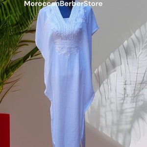 May include: White kaftan with white embroidery. The kaftan has a V-neck and short sleeves. The embroidery is intricate and detailed. MoroccanBerberStore is printed on the top of the image.