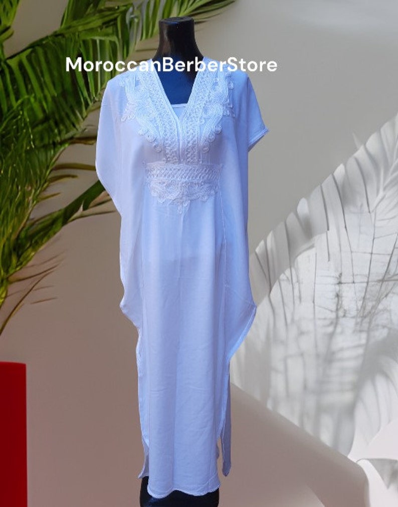 May include: White kaftan with white embroidery. The kaftan has a V-neck and short sleeves. The embroidery is intricate and detailed. MoroccanBerberStore is printed on the top of the image.