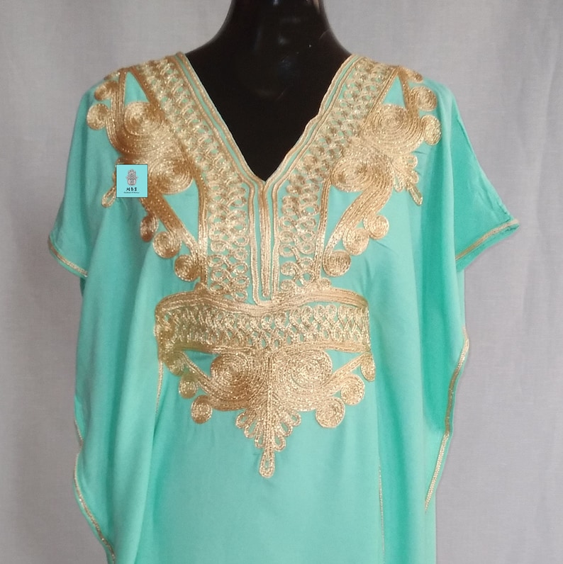 Puede incluir: Una kaft&aacute;n turquesa con bordados dorados. El bordado es intrincado y presenta un dise&ntilde;o floral. La kaft&aacute;n tiene cuello en V y mangas cortas.
