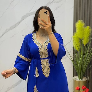 May include: A royal blue maxi dress with gold embroidery and tassel details. The dress has a V-neckline and long sleeves.