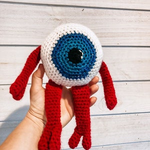 May include: A crocheted eye monster toy with a white body, blue and black eye, and red arms and legs.