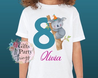 Könnte beinhalten: Weißes T-Shirt mit einer blauen Zahl 8, einem Koala mit Partyhut und dem Namen Olivia in Pink.