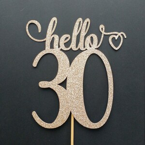 May include: Gold glitter cake topper with the text "hello" and a heart, and the number "30".