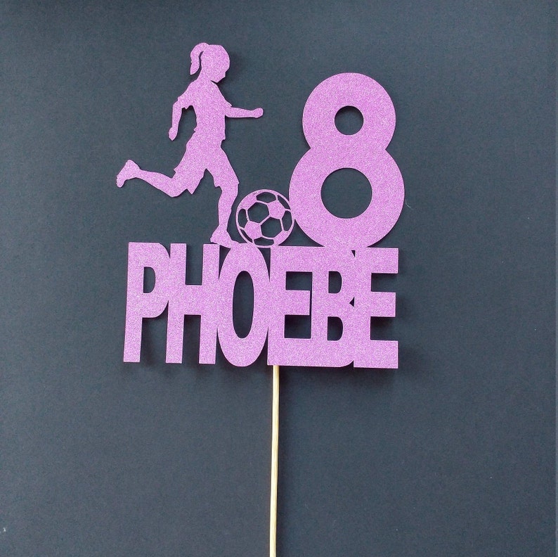 May include: Purple glitter cake topper with a silhouette of a girl playing soccer, the number 8, and the name "PHOEBE".