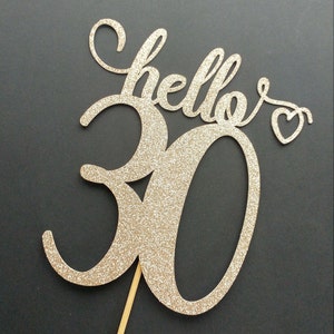 May include: Gold glitter cake topper with the words "hello 30" and a small heart.