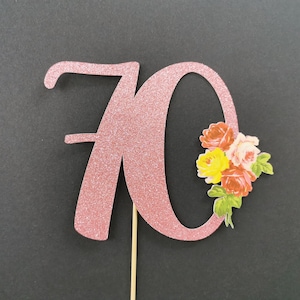 Puede incluir: Topper de pastel de purpurina rosa con el número 70 y un diseño floral. Las flores son rojas, amarillas y rosas.