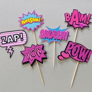 May include: Six colourful cardboard photo booth props with stick handles. The props feature the words "BAM!" in pink, "POW!" in pink, "ZAP!" in pink and white, "WOW!" in pink, "SMASH!" in blue and pink, and "AWESOME!" in yellow and blue.