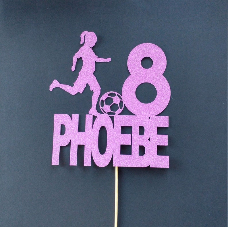 May include: Purple glitter cake topper with a silhouette of a girl playing soccer, the number 8, and the name "PHOEBE".