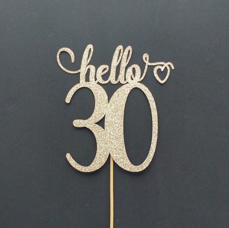 May include: Gold glitter cake topper with the text "hello" and a heart, and the number "30" in a cursive font.