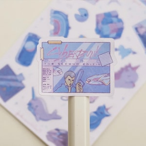 May include: A sticker featuring a retro-style illustration with the text "Cyberpunk 2033, The Second Edition." The sticker has a blue and purple color scheme, with images of a person holding a gun and a futuristic vehicle. Other stickers are visible in the background.