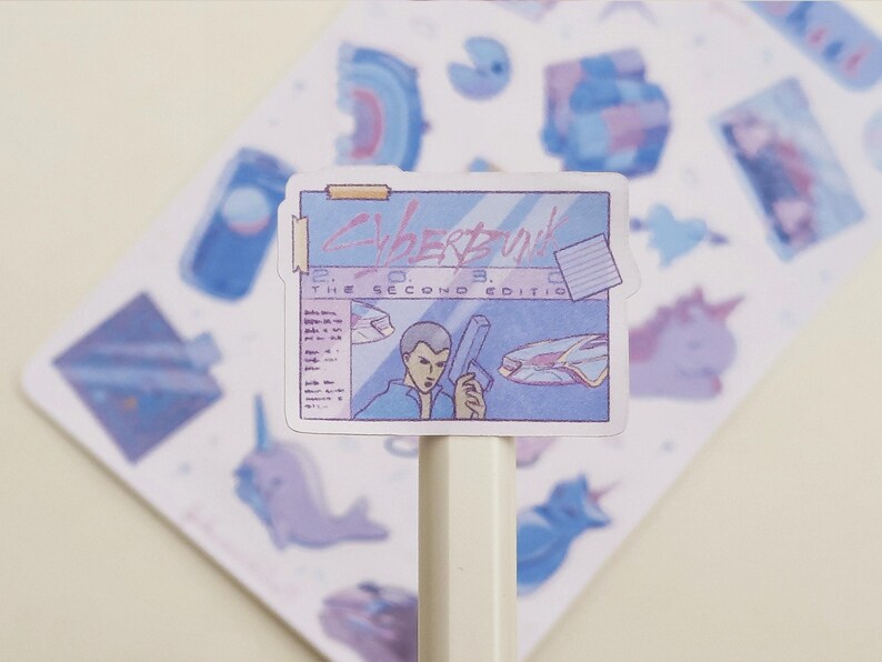 May include: A sticker featuring a retro-style illustration with the text "Cyberpunk 2033, The Second Edition." The sticker has a blue and purple color scheme, with images of a person holding a gun and a futuristic vehicle. Other stickers are visible in the background.