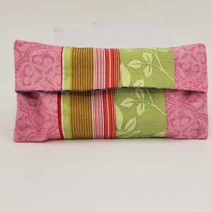 May include: A pink and green fabric tissue holder with a floral pattern. The holder is folded closed and has a striped design on the front.