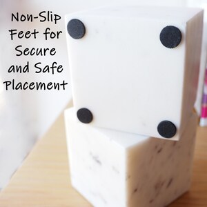 Op de afbeelding: Twee witte vierkante dozen met zwarte antislipvoetjes aan de onderkant. De dozen zijn op elkaar gestapeld. De tekst "Non-Slip Feet for Secure and Safe Placement" staat aan de linkerkant van de afbeelding.
