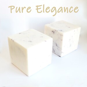 Op de afbeelding: Twee witte marmeren kubussen met een gespikkeld patroon. De kubussen staan op een wit oppervlak. De tekst "Pure Elegance" is in goud boven de kubussen geschreven.