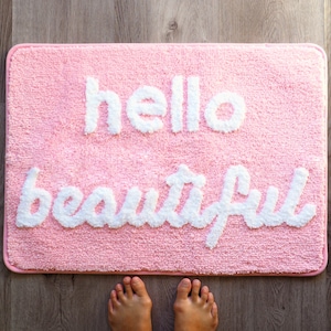 May include: Pink bath mat with white fluffy lettering that reads "hello beautiful".