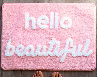 May include: Pink bath mat with white fluffy lettering that reads "hello beautiful".