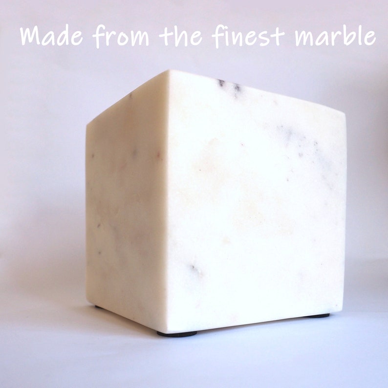 Op de afbeelding: Een witte marmeren kubus met een glad, gepolijst oppervlak. De kubus heeft een subtiele grijze adering. De kubus staat op een wit oppervlak. "Made from the finest marble" staat in zwarte tekst bovenaan de afbeelding.
