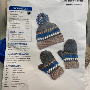 May include: Crochet pattern for a hat, mittens, and headband. The pattern uses bulky weight yarn in grey, light brown, blue, and off-white. The pattern includes instructions for sizes J-10 (6.0 mm) and L-11 (8.0 mm) crochet hooks. The pattern is for one size that fits most.