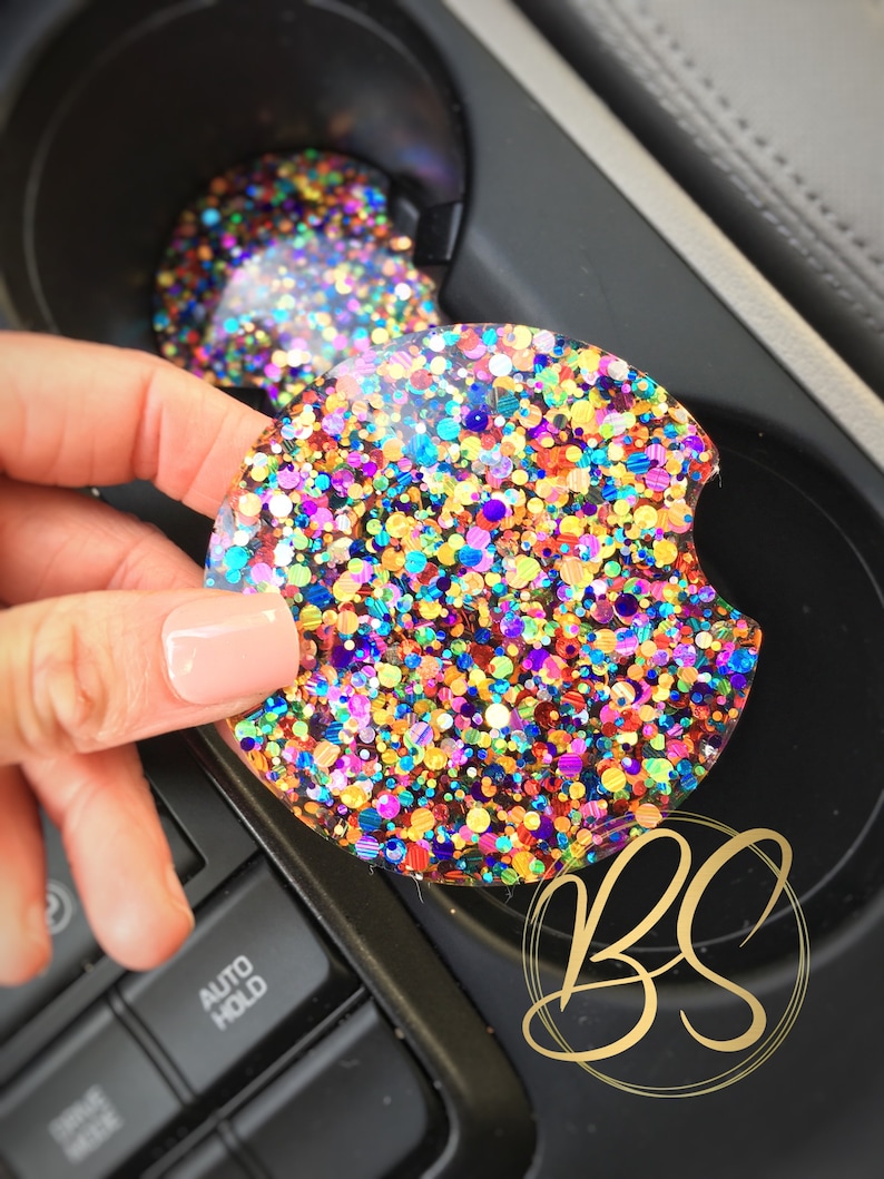 May include: A colorful glitter car coaster with a variety of colors including red, orange, yellow, green, blue, purple, and gold. The coaster is round and has a glossy finish.