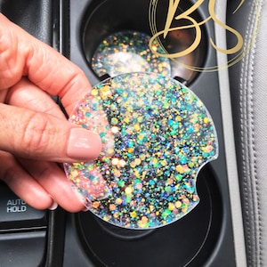 May include: A clear cup holder with a colourful glitter design. The cup holder is made of resin and has a black background with iridescent glitter.