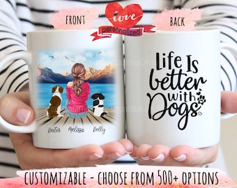 May include: White ceramic mug featuring a personalized illustration of a person with two dogs on a dock, with mountains and water in the background. The back of the mug says "Life Is better with Dogs".