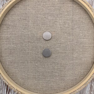 May include: Two round silver magnetic buttons on a beige burlap background.