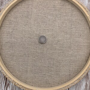 Peut inclure: Un cercle &agrave; broder rond en bois avec un tissu en lin naturel tendu au centre. Un petit bouton de couleur argent&eacute;e est centr&eacute; sur le tissu.