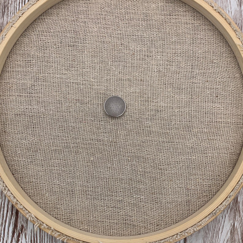 Peut inclure: Un cercle &agrave; broder rond en bois avec un tissu en lin naturel tendu au centre. Un petit bouton de couleur argent&eacute;e est centr&eacute; sur le tissu.