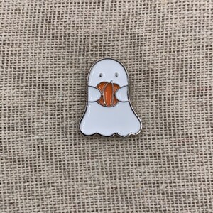 Peut inclure: Un fant&ocirc;me blanc tenant une citrouille orange dans ses mains. Le fant&ocirc;me a un petit visage amical avec deux yeux noirs et une petite bouche.