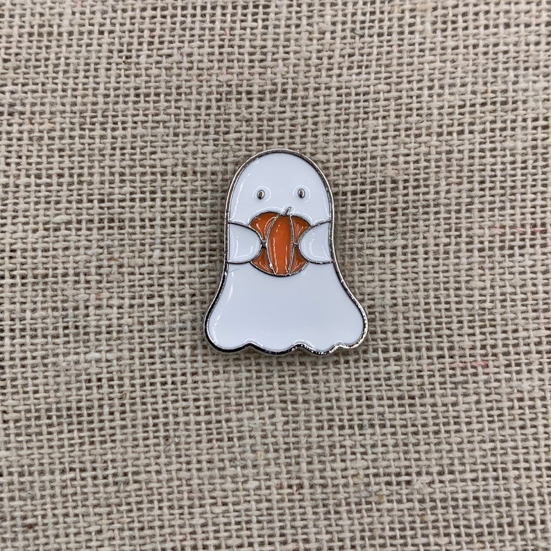 Peut inclure: Un fant&ocirc;me blanc tenant une citrouille orange dans ses mains. Le fant&ocirc;me a un petit visage amical avec deux yeux noirs et une petite bouche.