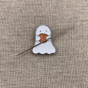 Peut inclure: Un fant&ocirc;me blanc avec un visage amical tenant une petite citrouille orange. Le fant&ocirc;me est attach&eacute; &agrave; une aiguille argent&eacute;e.