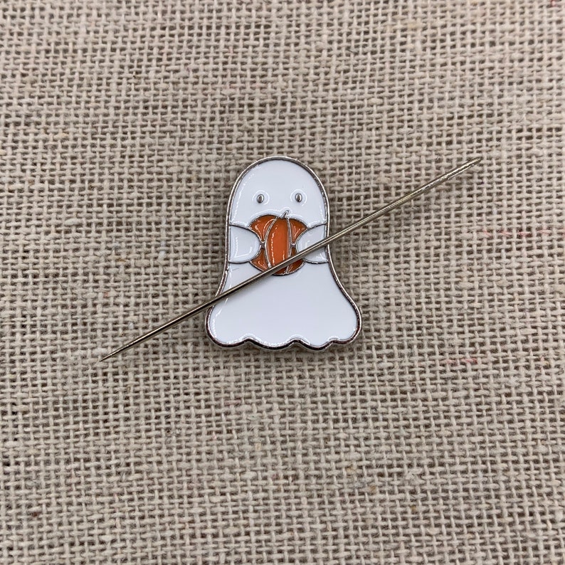 Peut inclure: Un fant&ocirc;me blanc avec un visage amical tenant une petite citrouille orange. Le fant&ocirc;me est attach&eacute; &agrave; une aiguille argent&eacute;e.
