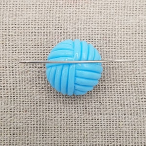 May include: A light blue plastic yarn ball with a silver knitting needle going through the center.