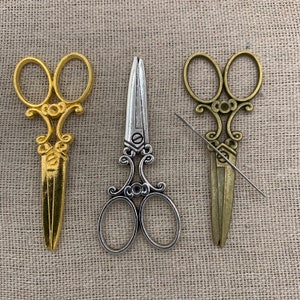 May include: Three pairs of decorative scissors with ornate handles. The scissors are gold, silver, and bronze.